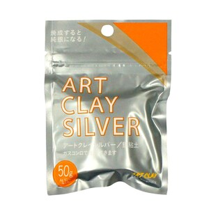 May include: A silver-colored, rectangular, flexible pouch containing 50g of Art Clay Silver. The packaging features the text ART CLAY SILVER in large letters, an orange corner accent, and Japanese characters printed on the front surface.