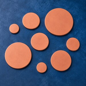 May include: A collection of eight circular copper-coloured discs of varying sizes arranged in a scattered pattern. Each disc features a smooth, flat surface with a metallic finish, ranging from small to large diameters across the composition.