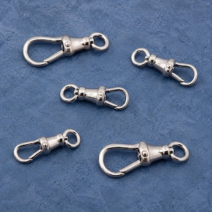 May include: Five silver-toned metal swivel lobster claw clasps arranged on a textured blue surface. Each clasp features a spring-loaded gate mechanism and a circular loop at the base for attachment, showcasing a polished, reflective metallic finish.