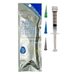 May include: A silver-colored foil pouch labeled Art Clay Silver with a 10g weight indicator, accompanied by a clear plastic syringe with a white plunger and three interchangeable nozzle tips in green, blue, and gray colors for precision application.