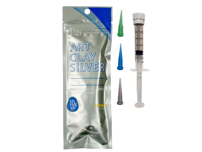 May include: A silver-colored foil pouch labeled Art Clay Silver with a 10g weight indicator, accompanied by a clear plastic syringe with a white plunger and three interchangeable nozzle tips in green, blue, and gray colors for precision application.