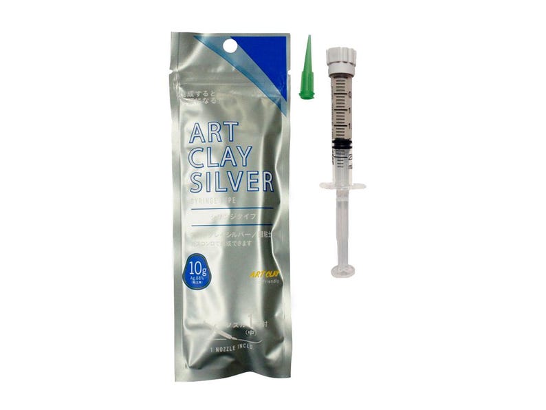 May include: A 10g package of Art Clay Silver in a silver metallic pouch with blue accents, featuring the text Art Clay Silver. Beside it is a clear plastic syringe filled with silver clay, a white plunger, and a separate small green nozzle tip.