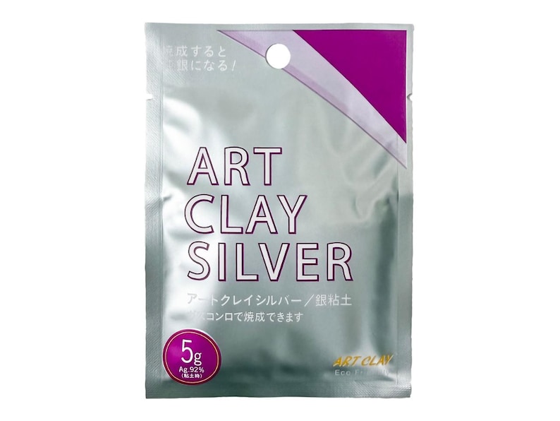 May include: A silver-colored rectangular packet of Art Clay Silver, featuring purple accents and a circular hang hole at the top. The front displays the text Art Clay Silver, 5g, and Ag.92% in clear lettering, indicating a 5-gram weight of silver clay.