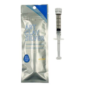May include: A silver-colored foil pouch labeled ART CLAY SILVER with a 10g weight indicator and a clear plastic syringe containing a gray paste. The syringe features a white plunger and a graduated scale printed on the side of the barrel.