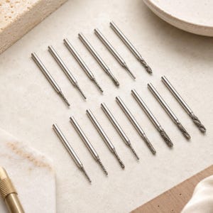 May include: A set of fourteen silver-coloured metal drill bits with textured, abrasive tips. Each bit features a smooth cylindrical shank that transitions into a thinner, grit-coated working end designed for precision drilling or engraving tasks.