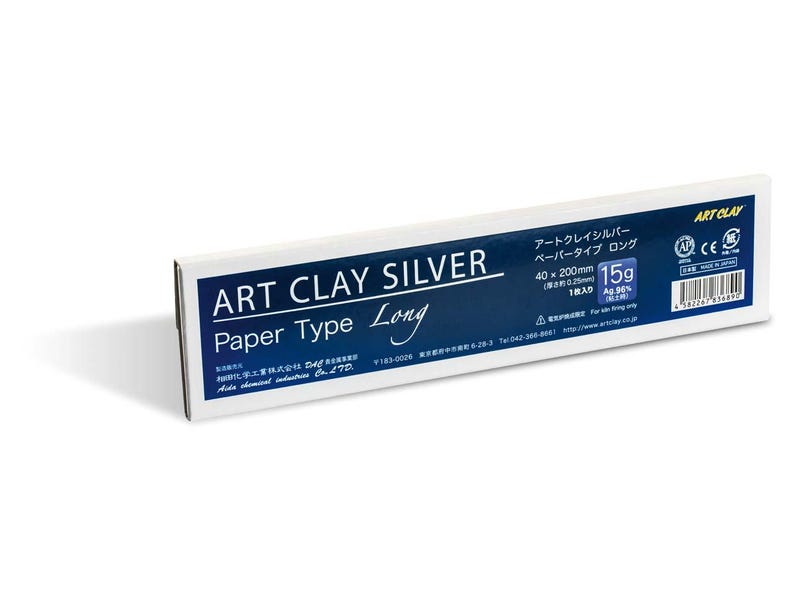 May include: A rectangular white and dark blue box of Art Clay Silver Paper Type Long. The packaging displays the text Art Clay Silver, 15g, 40 x 200mm, and 0.25mm thickness. It includes a barcode, manufacturer details, and certification logos.