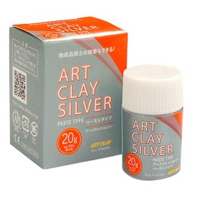 May include: A 20g container of Art Clay Silver paste type and its matching rectangular cardboard box. The packaging is grey and orange with white text that reads Art Clay Silver, Paste Type, and 20g. The container has a white screw-on lid.