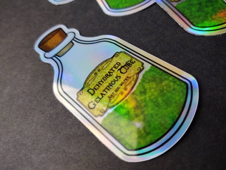 May include: A holographic sticker of a glass bottle containing a green, mossy substance. The label reads "Dehydrated Gelatinous Cube, Just Add Water".