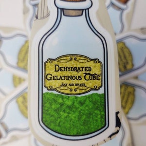 May include: A sticker of a glass bottle with a cork stopper. The bottle is filled with a green powder and has a label that reads "Dehydrated Gelatinous Cube" and "Just Add Water".