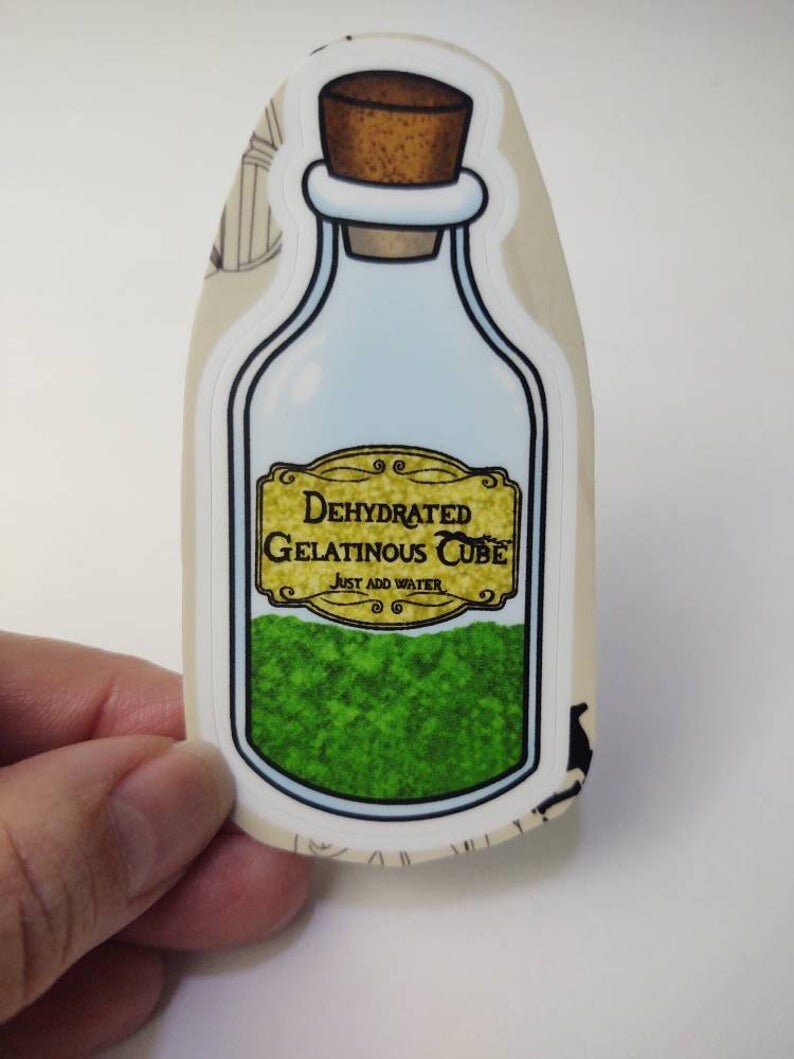 May include: A sticker of a glass bottle with a cork stopper. The bottle contains a green powder and has a label that reads "Dehydrated Gelatinous Cube, Just Add Water".