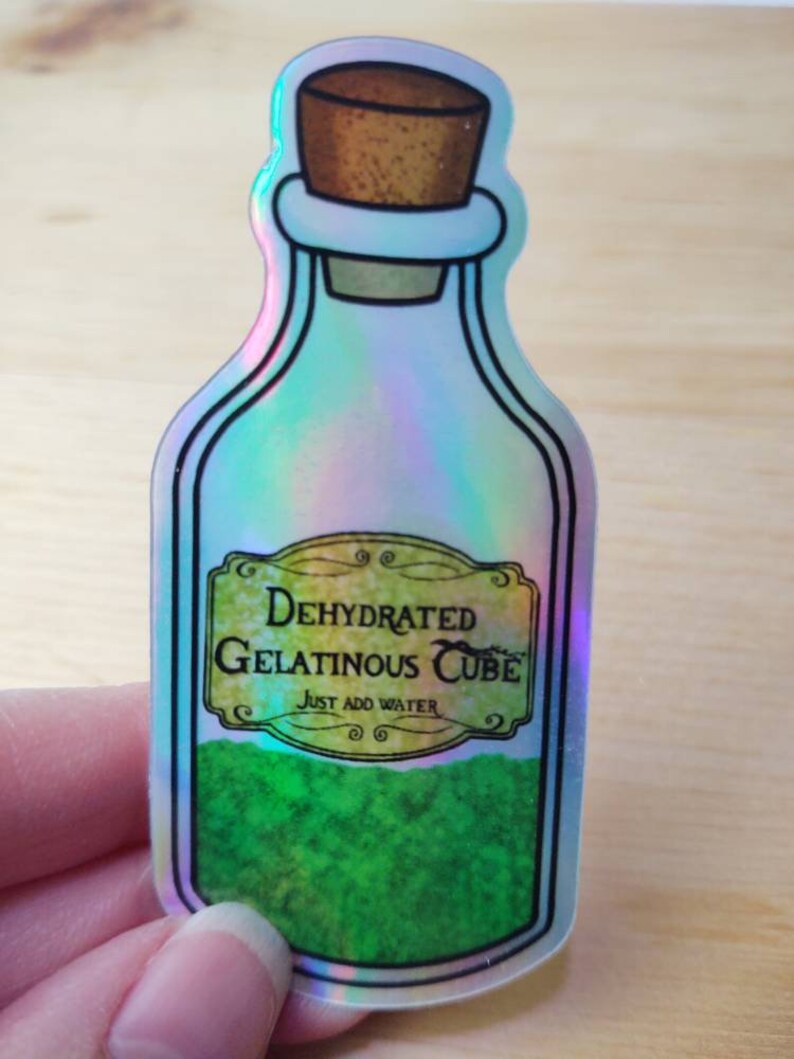 May include: A holographic sticker of a glass bottle with a cork stopper. The bottle is filled with a green substance and has a label that reads "Dehydrated Gelatinous Cube" and "Just Add Water".
