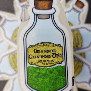 May include: A sticker of a glass bottle with a cork stopper. The bottle is filled with green gelatinous cubes and has a label that reads "Dehydrated Gelatinous Cube. Just Add Water."
