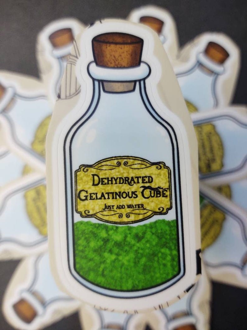 May include: A sticker of a glass bottle with a cork stopper. The bottle is filled with green gelatinous cubes and has a label that reads "Dehydrated Gelatinous Cube. Just Add Water."