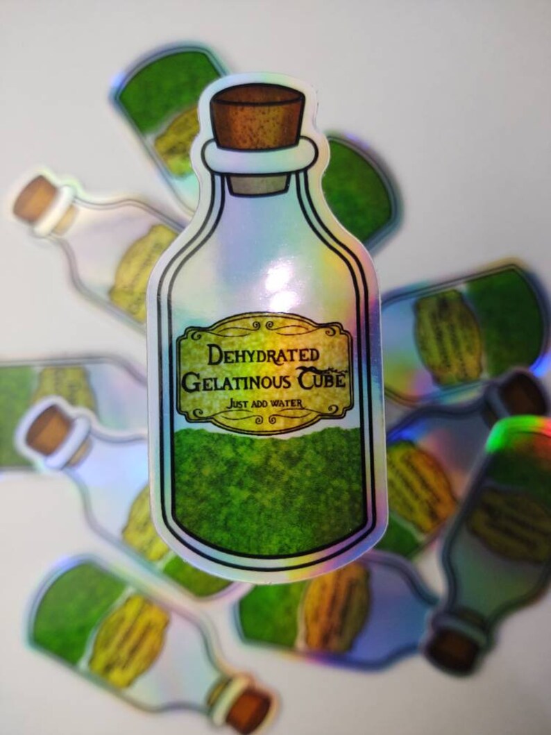 May include: A holographic sticker of a green glass bottle with a cork stopper. The label reads "Dehydrated Gelatinous Cube, Just Add Water".