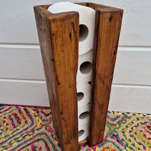 May include: A rustic wooden toilet paper holder with a dark brown stain. The holder is designed to hold four rolls of toilet paper.