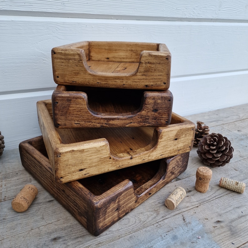 K&ouml;nnte beinhalten: Vier Holztabletts, die &uuml;bereinander gestapelt sind. Die Tabletts sind aus recyceltem Holz gefertigt und haben einen rustikalen, abgenutzten Look. Jedes Tablett hat einen erh&ouml;hten Rand und einen Ausschnitt in der Mitte. Die Tabletts sind perfekt zum Organisieren und Pr&auml;sentieren von Gegenst&auml;nden.