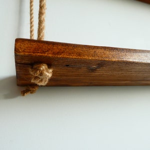 K&ouml;nnte beinhalten: Ein Holzregal mit einer dunkelbraunen Beize, das an zwei dicken Seilen mit Knoten an den Enden h&auml;ngt.