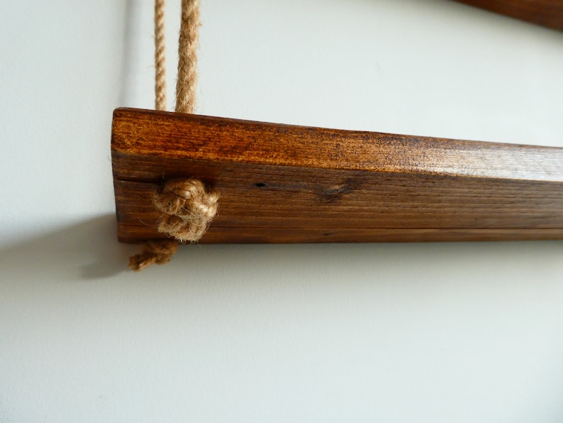 K&ouml;nnte beinhalten: Ein Holzregal mit einer dunkelbraunen Beize, das an zwei dicken Seilen mit Knoten an den Enden h&auml;ngt.