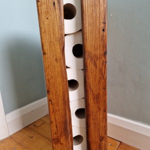 May include: A rustic wooden toilet paper holder with a dark brown stain. The holder has four slots for toilet paper rolls.