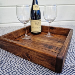 May include: A dark brown wooden serving tray with two wine glasses and a bottle of wine on top. The tray is sitting on a blue and white patterned surface.