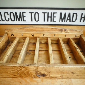 May include: Wooden box with seven compartments labeled M, T, W, T, F, S, S. The box is made of natural wood with a rustic finish.