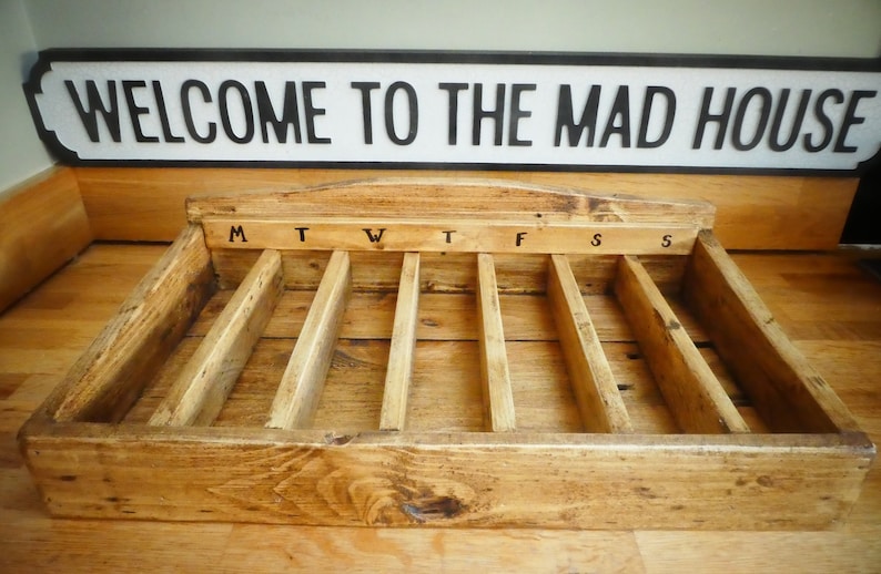 May include: Wooden box with seven compartments labeled M, T, W, T, F, S, S. The box is made of natural wood with a rustic finish.