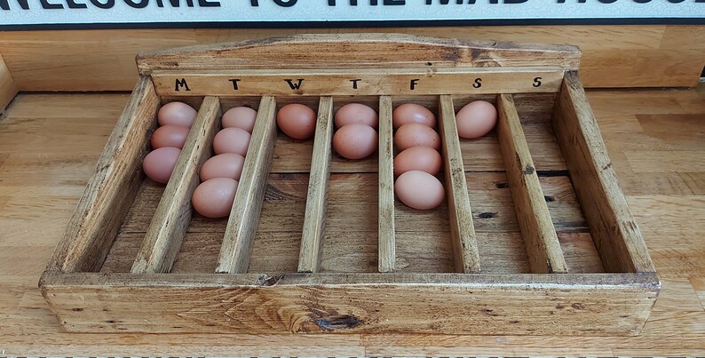 May include: A wooden egg tray with 10 brown eggs, labeled with the days of the week: M, T, W, T, F, S, S.