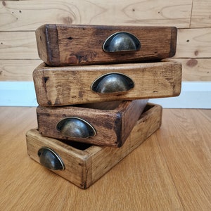 May include: Four wooden trays stacked on top of each other. Each tray has a metal handle and a dark brown stain. The trays are on a wooden surface.