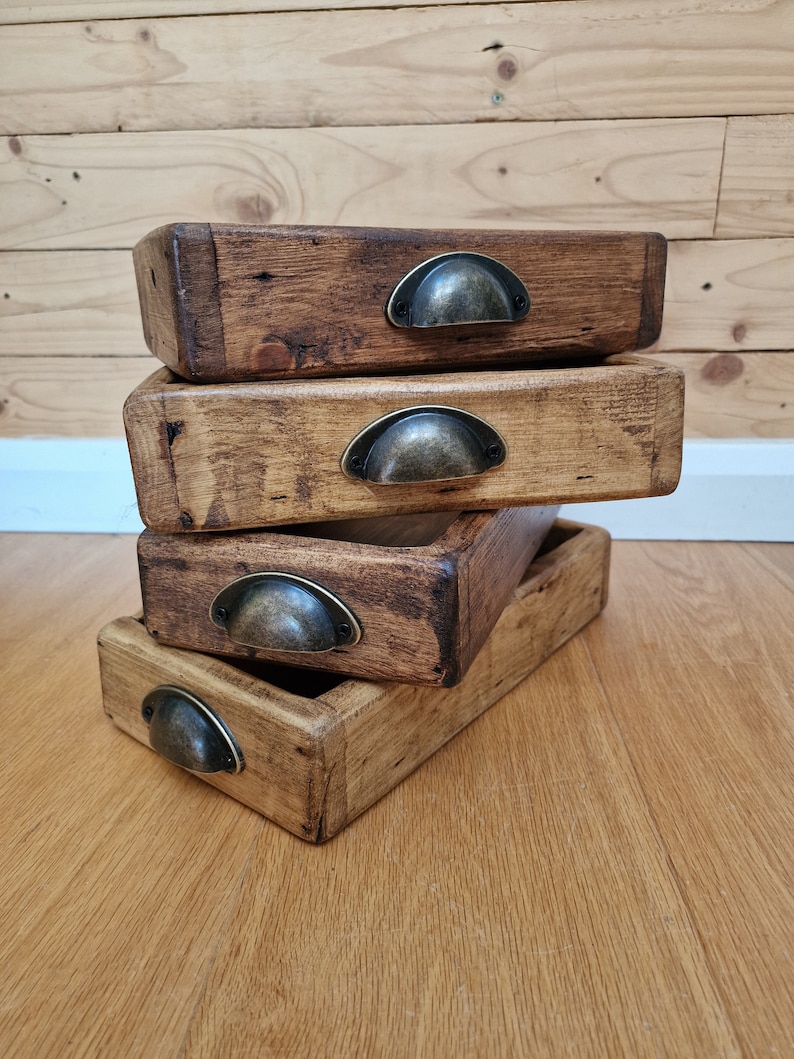 May include: Four wooden trays stacked on top of each other. Each tray has a metal handle and a dark brown stain. The trays are on a wooden surface.