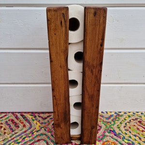 May include: A wooden toilet paper holder with a rustic brown finish. The holder can store five rolls of toilet paper.