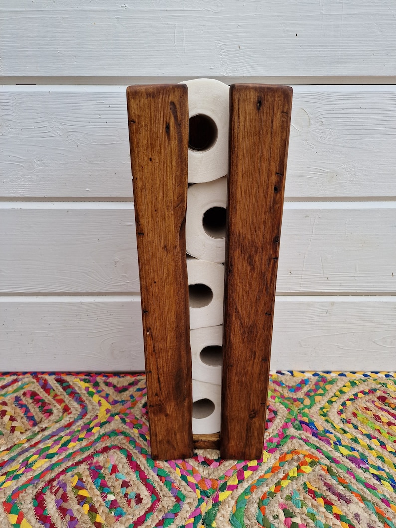 May include: A wooden toilet paper holder with a rustic brown finish. The holder can store five rolls of toilet paper.