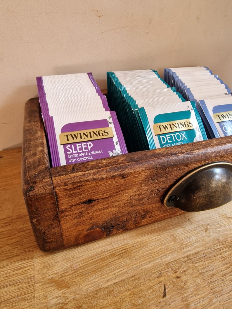 May include: A wooden tea bag organizer with a metal handle. The organizer is filled with boxes of Twinings tea bags. The tea flavors are Sleep, Spiced Apple & Vanilla with Camomile, Detox, Lemon & Ginger.