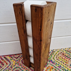 May include: A rustic wooden toilet paper holder with a dark brown stain. The holder is designed to hold four rolls of toilet paper.