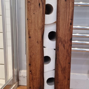 May include: A rustic wooden toilet paper holder with four rolls of toilet paper inside. The holder is made of dark brown wood with a natural finish.