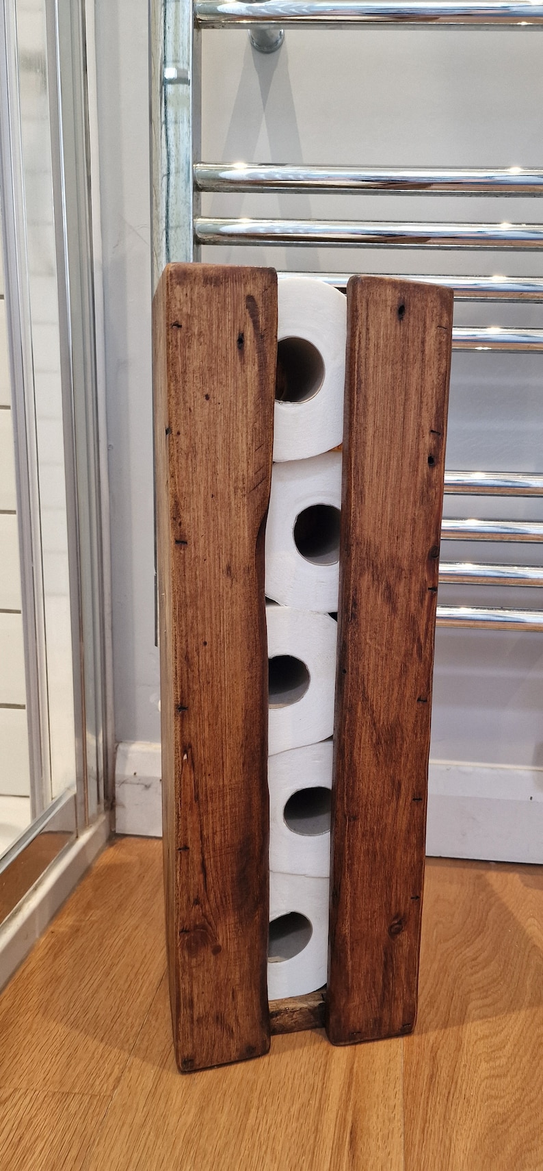 May include: A rustic wooden toilet paper holder with four rolls of toilet paper inside. The holder is made of dark brown wood with a natural finish.