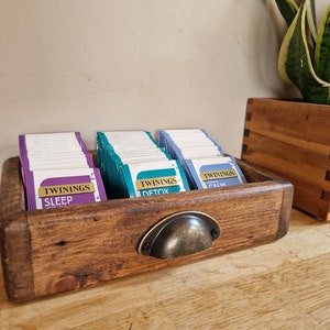 May include: A wooden tea bag organizer with a metal handle. The organizer has three compartments filled with tea bags labeled "Twinings Sleep", "Twinings Detox", and "Twinings Calm".