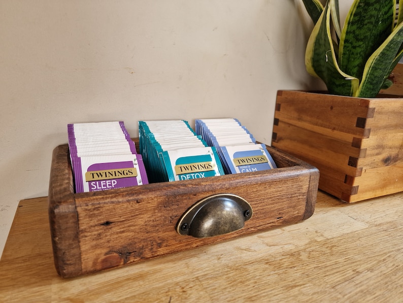 May include: A wooden tea bag organizer with a metal handle. The organizer has three compartments filled with tea bags labeled "Twinings Sleep", "Twinings Detox", and "Twinings Calm".