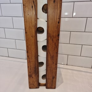 May include: A wooden toilet paper holder with four rolls of toilet paper. The holder is made of dark brown wood with a rustic finish.