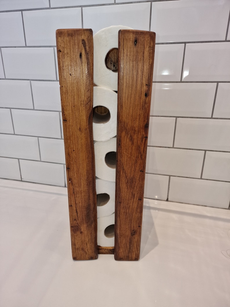 May include: A wooden toilet paper holder with four rolls of toilet paper. The holder is made of dark brown wood with a rustic finish.