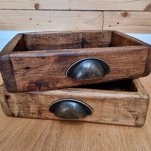 May include: Two wooden boxes with metal handles. The boxes are stacked on top of each other. The boxes are made of dark brown wood and have a rustic look.