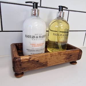 May include: Two bottles of Baylis & Harding hand and body lotion in a wooden tray. The bottles are labelled "Sweet Mandarin & Grapefruit" and "Sweet Almond". The tray is brown and has a rustic look.