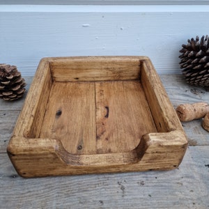 K&ouml;nnte beinhalten: Ein rustikaler Serviettenhalter aus Holz mit einer nat&uuml;rlichen Holzoptik. Der Halter hat eine rechteckige Form mit einem erh&ouml;hten Rand um die Kanten und einem Ausschnitt an der Vorderseite f&uuml;r einfachen Zugriff auf Servietten.