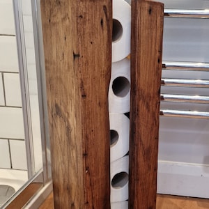 May include: A rustic wooden toilet paper holder with four rolls of toilet paper inside. The holder is made of dark brown wood with a natural finish.