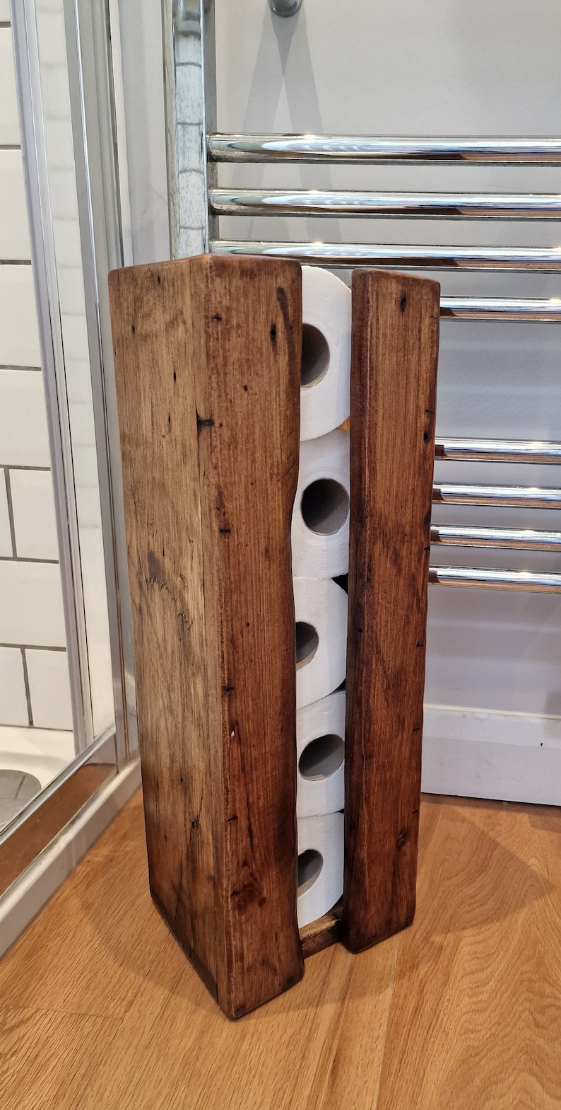 May include: A rustic wooden toilet paper holder with four rolls of toilet paper inside. The holder is made of dark brown wood with a natural finish.