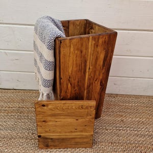 May include: A wooden storage box with a blanket draped over the top. The box is made of reclaimed wood and has a rustic finish. The blanket is white with blue stripes.
