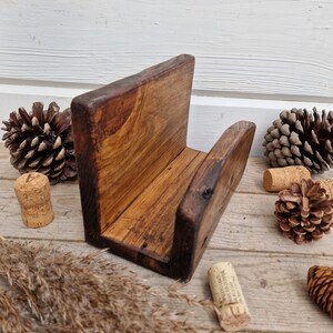 May include: A rustic wooden phone stand with a dark brown stain. The stand has a simple design with a single shelf and a back panel. The stand is made of reclaimed wood and has a natural, weathered look.