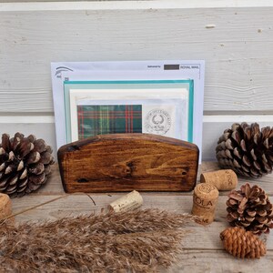 May include: A wooden letter holder with a rounded top, stained in a dark brown color. The holder is filled with envelopes and cards, including one with a green and red plaid pattern. A wax seal with a crest is visible on one of the envelopes. The text "Delivered by ROYAL MAIL" is visible on the top envelope.