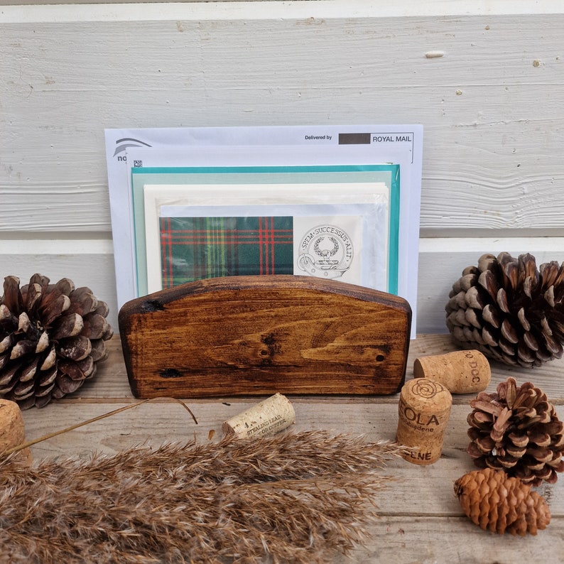 May include: A wooden letter holder with a rounded top, stained in a dark brown color. The holder is filled with envelopes and cards, including one with a green and red plaid pattern. A wax seal with a crest is visible on one of the envelopes. The text "Delivered by ROYAL MAIL" is visible on the top envelope.