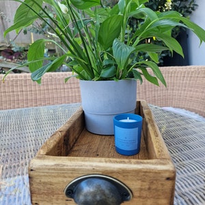 May include: A wooden tray with a metal handle, a potted plant, and a blue candle. The candle has the text "The little things we love each day" on the side.