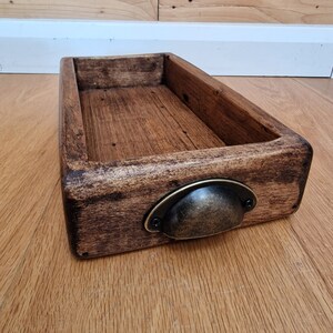 May include: A wooden tray with a dark brown stain and a metal handle. The tray has a rectangular shape and is made of wood.